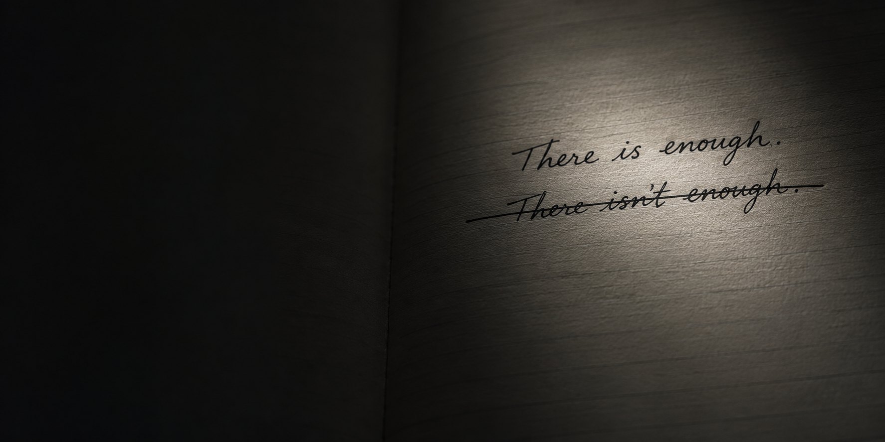 An open notebook in low light. The line &ldquo;There isn&rsquo;t enough.&rdquo; is struck through, and &ldquo;There is enough.&rdquo; is written above it in the same hand.